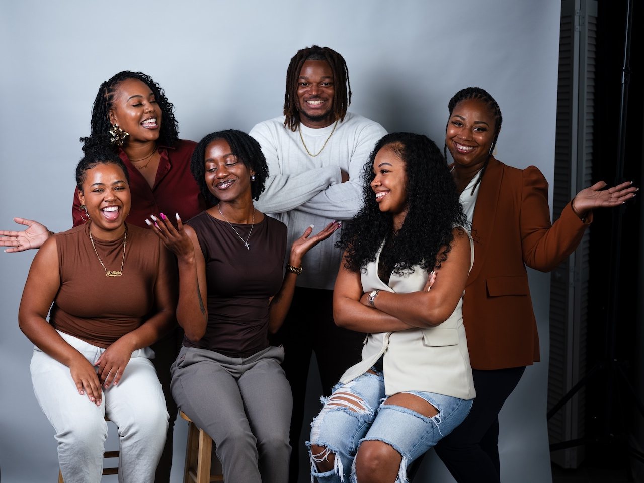 The Threshold Social founder and founding board together in a studio portrait, laughing — three seated on stools in front, three standing behind them.